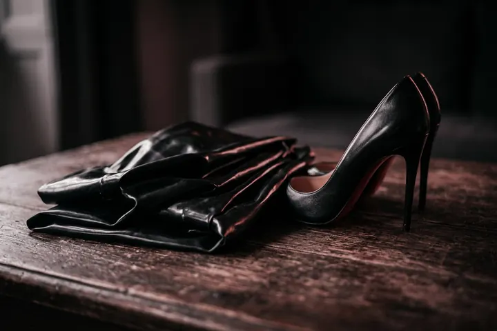 Tissu de latex noir plié à côté d'un escarpin à talon aiguille, éclairé en lumière rasante sur fond sombre